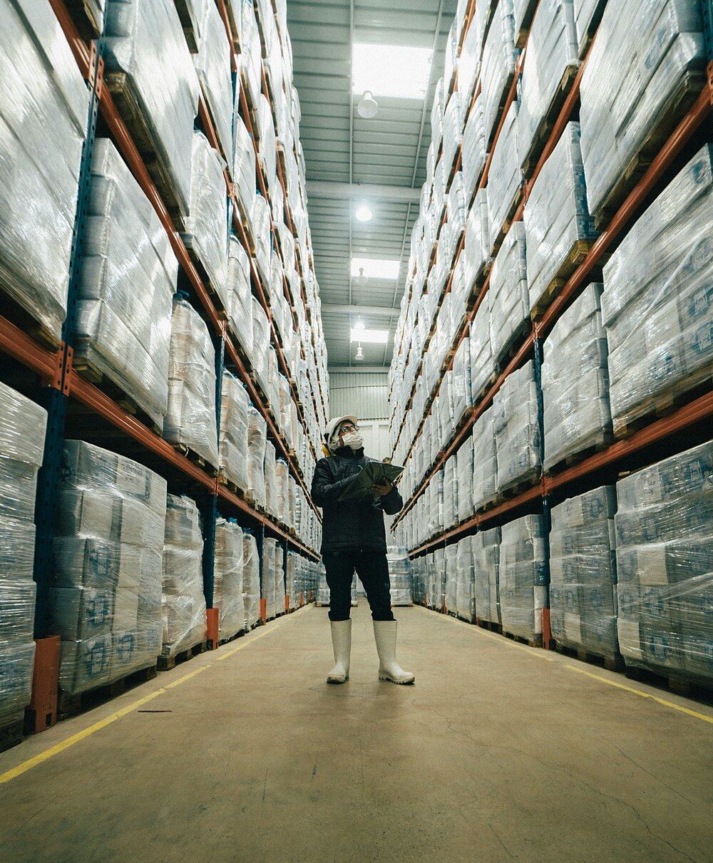 Warehouse operative in hard hat and hi-vis checking palletised stock against a clipboard